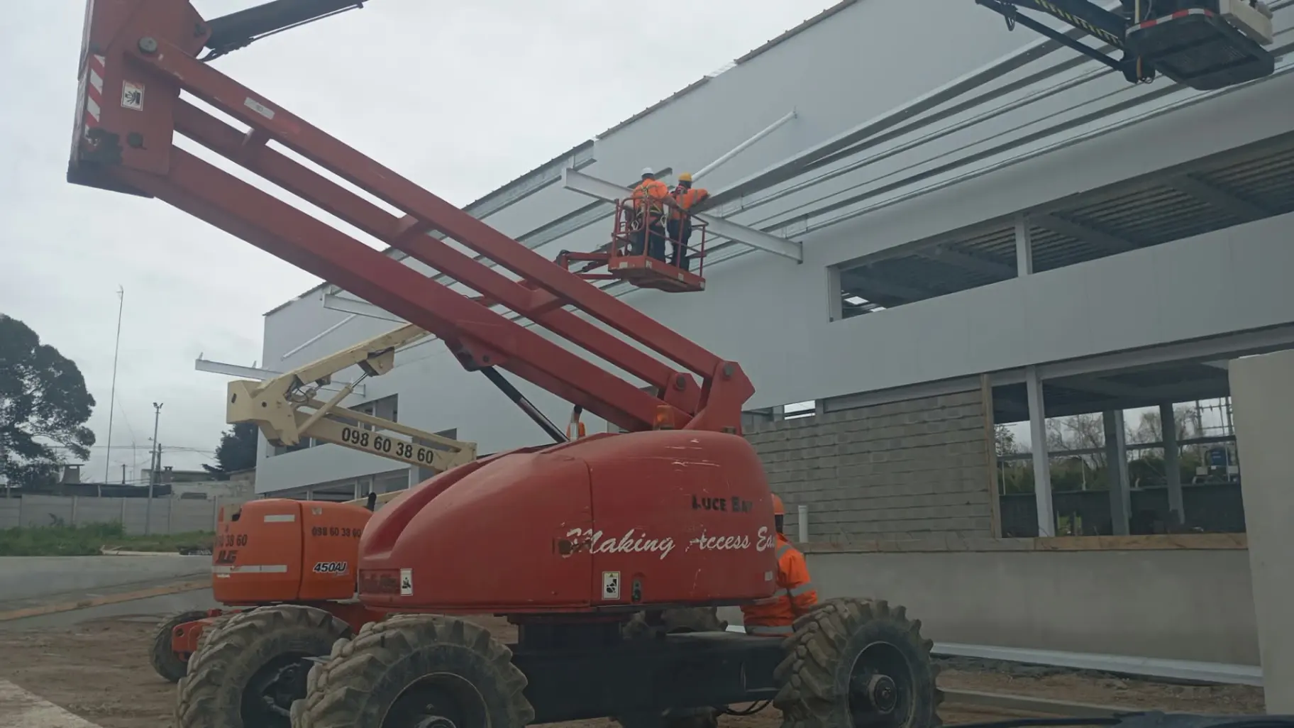 Plataforma elevadora articulada roja trabajando en techo de galpón industrial en Uruguay